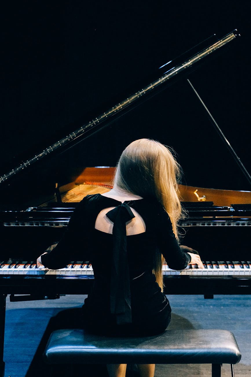 woman in black long sleeve dress sitting while playing a grand piano