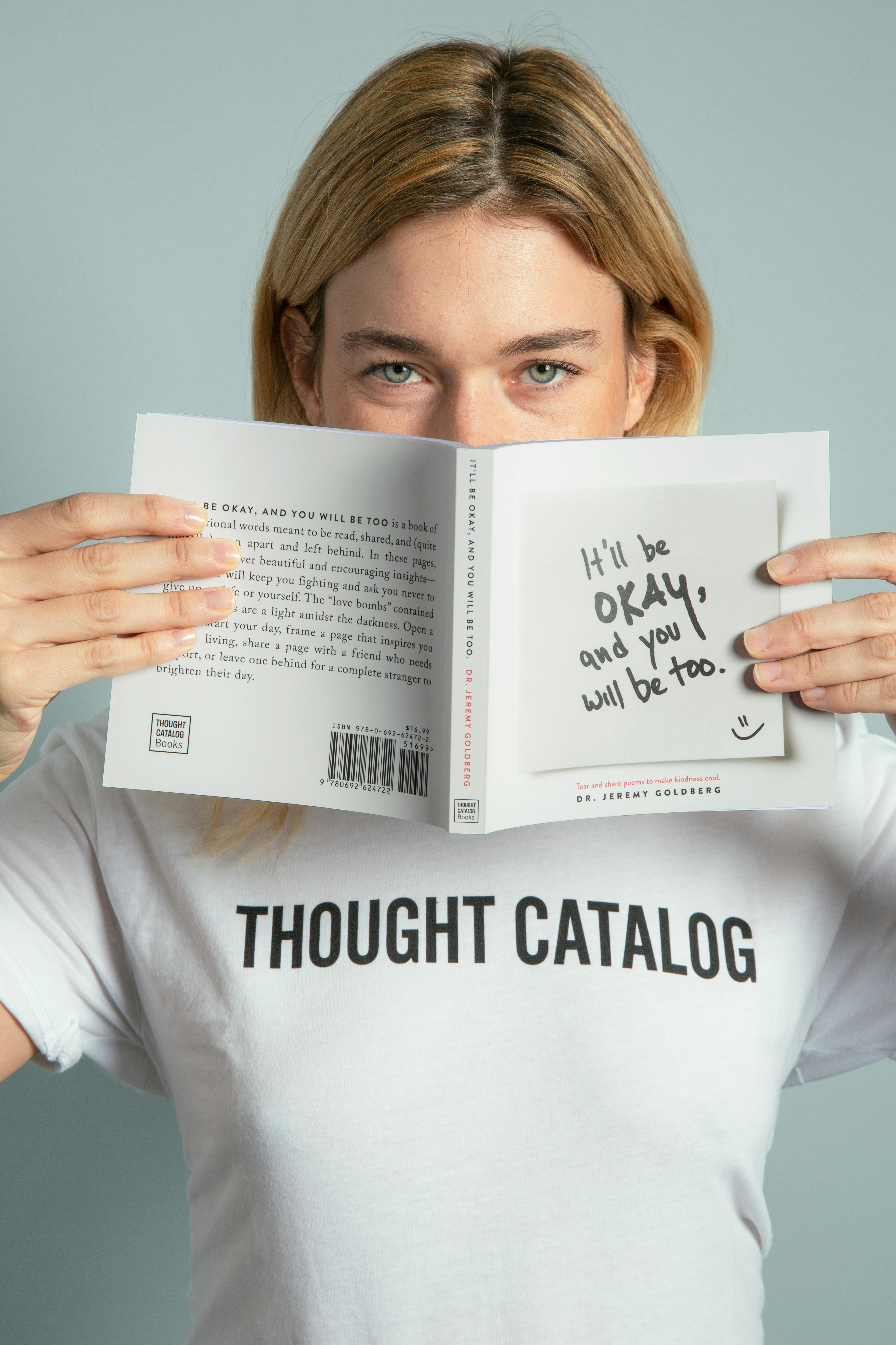 Woman holding a self-help book with the message “It’ll be okay, and you will be too” printed on the cover